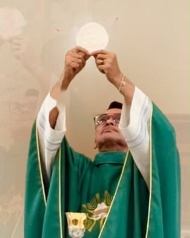 Padre Mauro Maia eleva a hóstia durante a missa, com casula verde